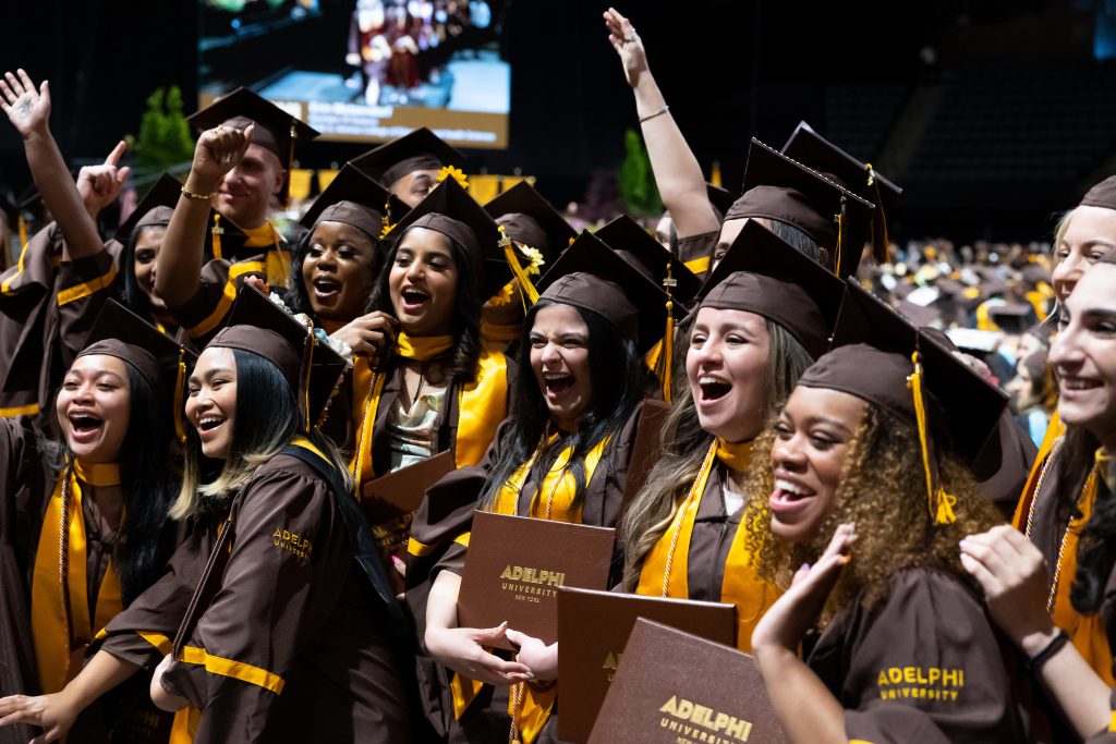 Group of individuals smiling wearing brown graduation gowns with yellow trimming. 