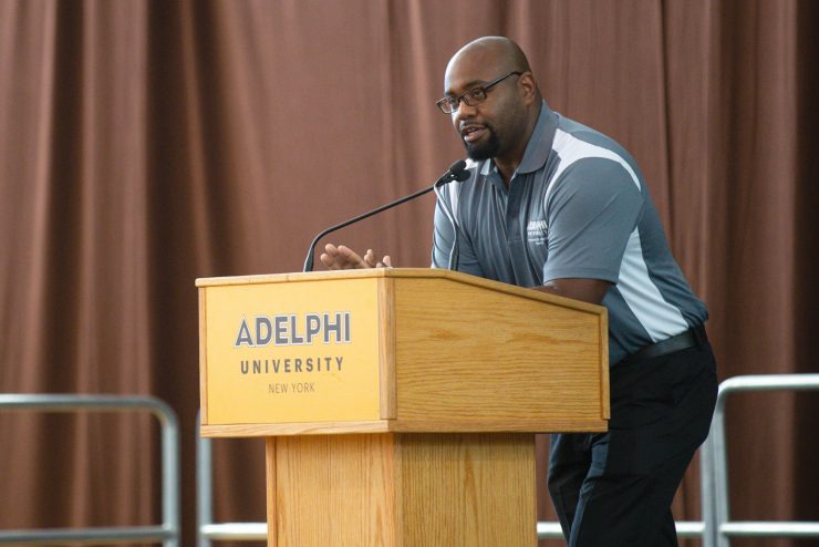 Guy Seneque speaking at a podium at Adelphi University