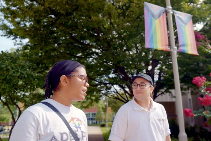Mena walking with a student on campus in front of pride flags