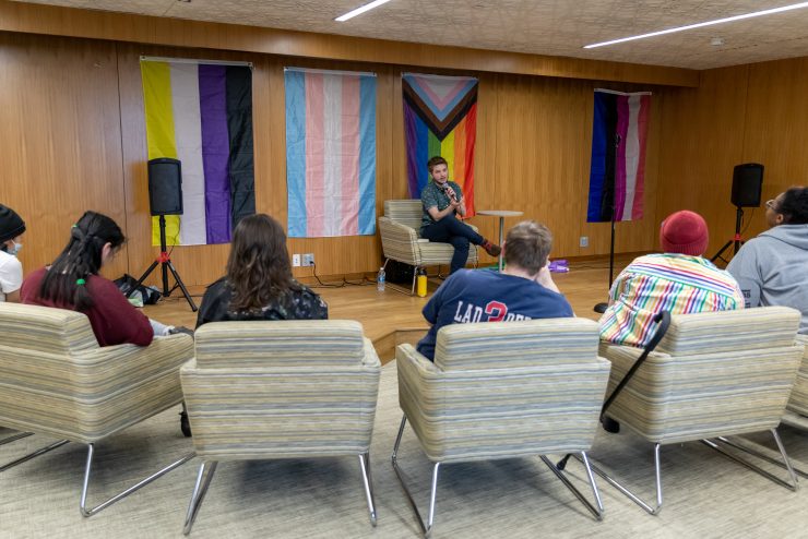 Jackson Bird speaking in front of an array of pride flags in front of Adelphi University students