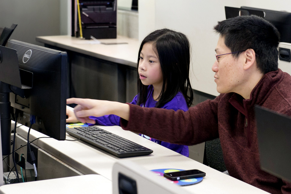 Adelphi university youth coding on our campus. A 4th grader works with faculty on a computer.