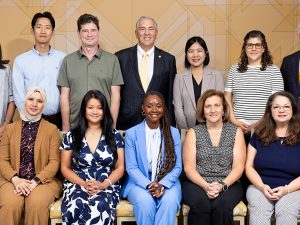 Group portrait of twelve new faculty members and a university administrator, arranged in two rows against a gold patterned wall.