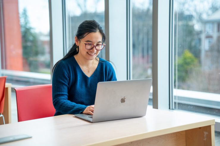 Professor Yiqi Zhu working on a laptop at Adelphi University