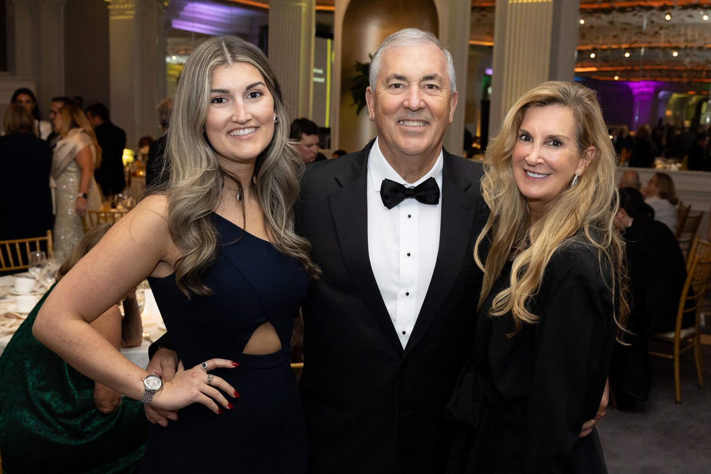 A man in a tuxedo, Chair of the Adelphi University Board of Trustees Michael Balboni ’81, JD, poses with two women in formal gowns.