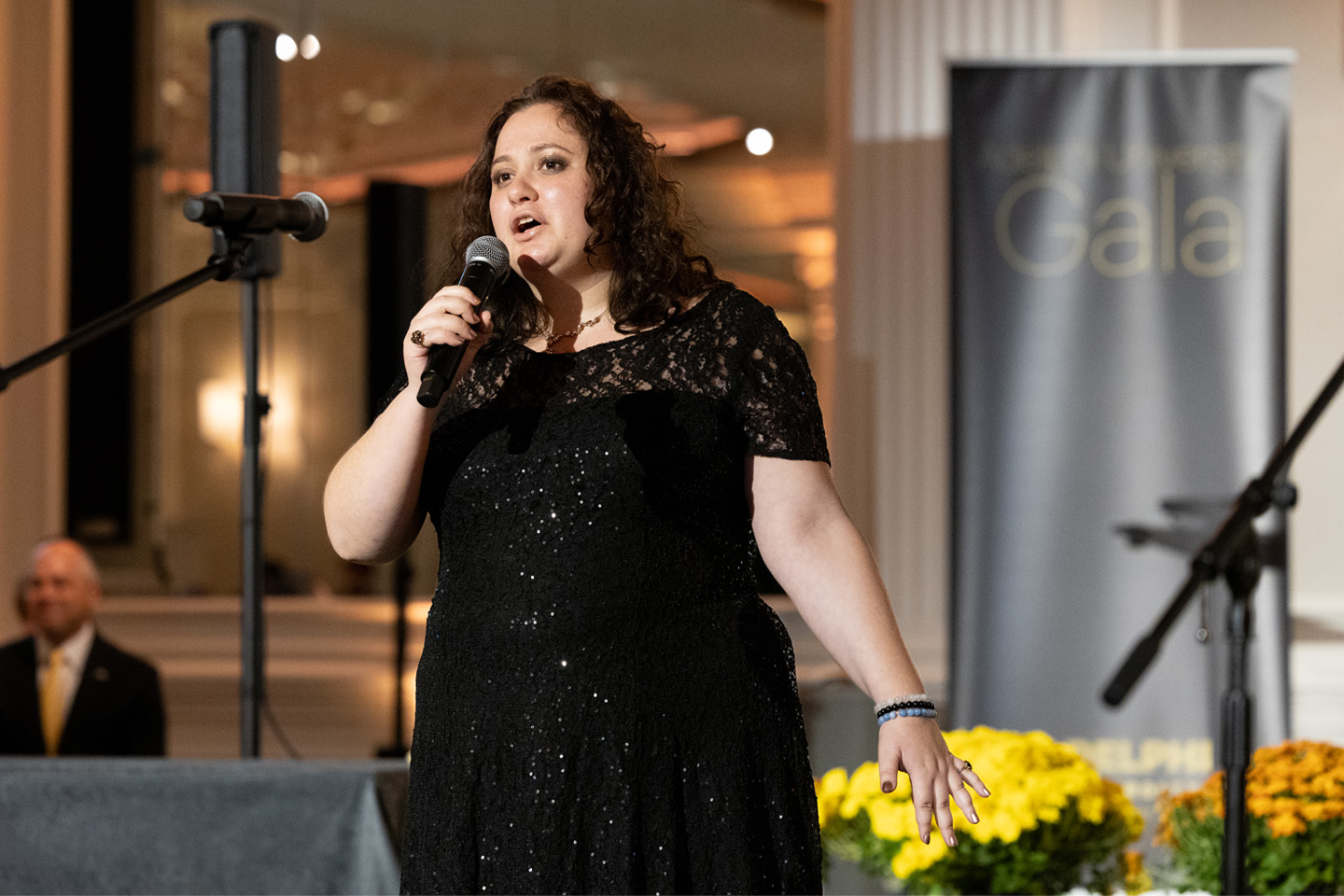 A woman in a black dress sings “There's a Place for Us” for the Gala crowd.