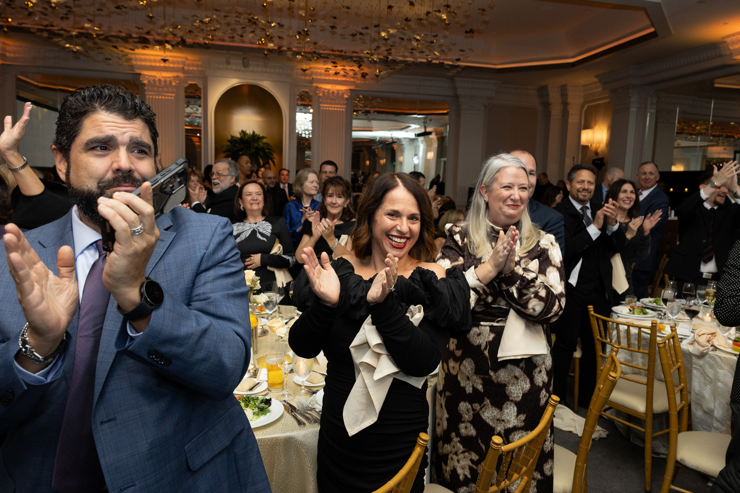 A large group of formally dressed individuals stand to clap for a performance.