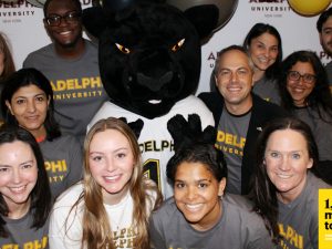 A group of smiling Adelphi employees and friends surround Paws, the Adelphi mascot