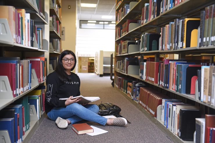 Carla Ojeda sits on the floor surrounded by books in the Swirbul Library