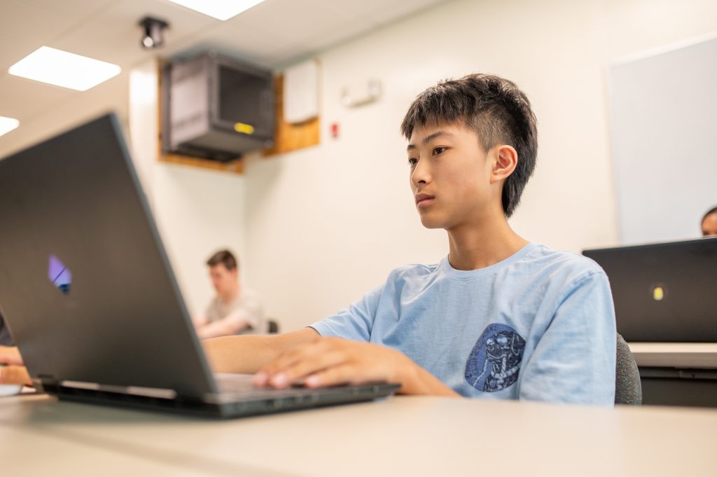 A student in Adelphi’s pre-college Computer Science & AI course works on coding and AI projects on his laptop.
