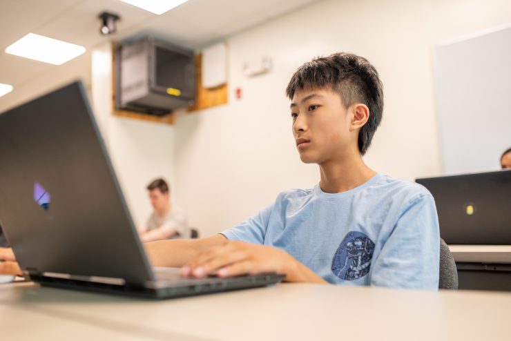 A student in Adelphi’s pre-college Computer Science & AI course works on coding and AI projects on his laptop.