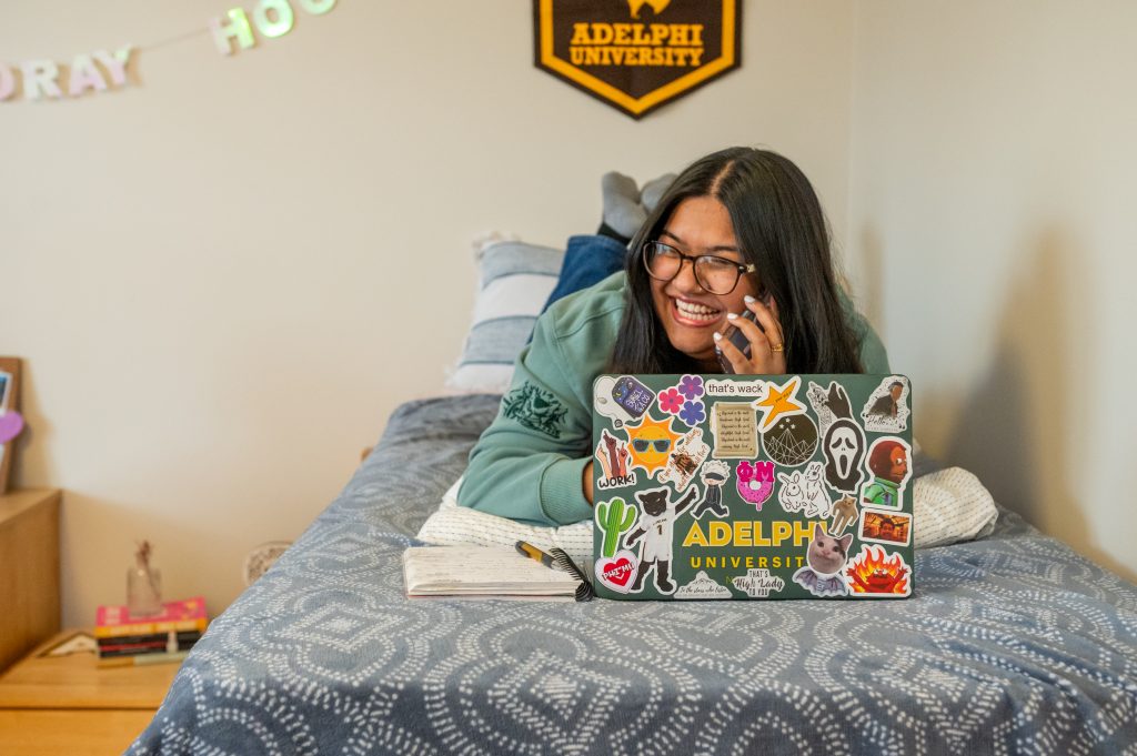 Residential life and housing dorm rooms - Student talking on phone while on her bed.
