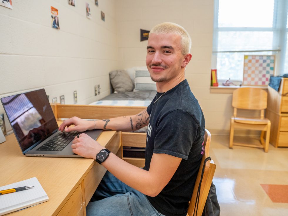 Student working at desk in a dorm room on Adelphi University campus.
