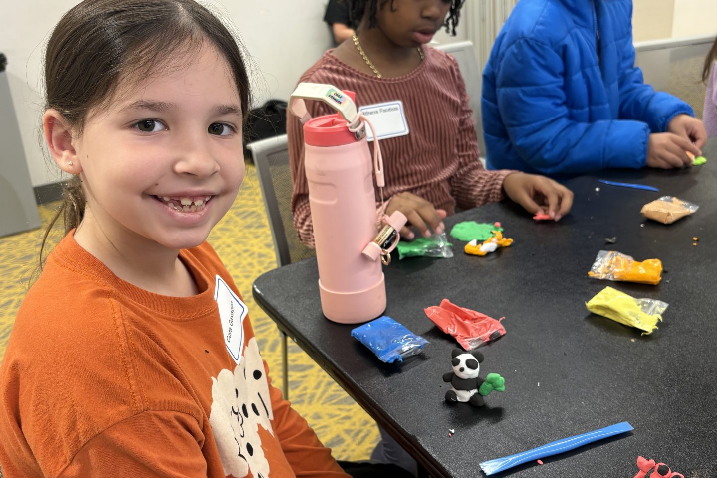 Adelphi employees’ child proudly presents her handcrafted clay sculptures, showcasing creativity and skill.