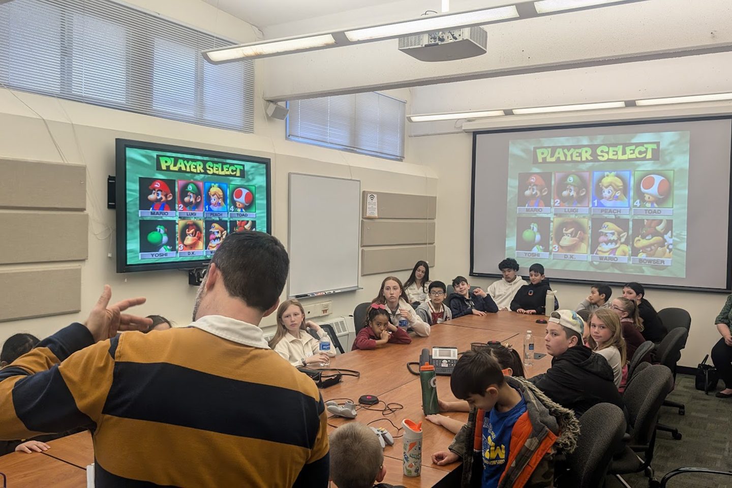 Children sitting around a conference room table with Mario Kart on large screens.