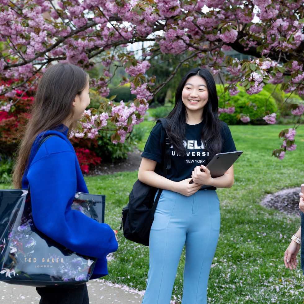International students talking together on Adelphi University's campus. Cherry blossoms in the background.