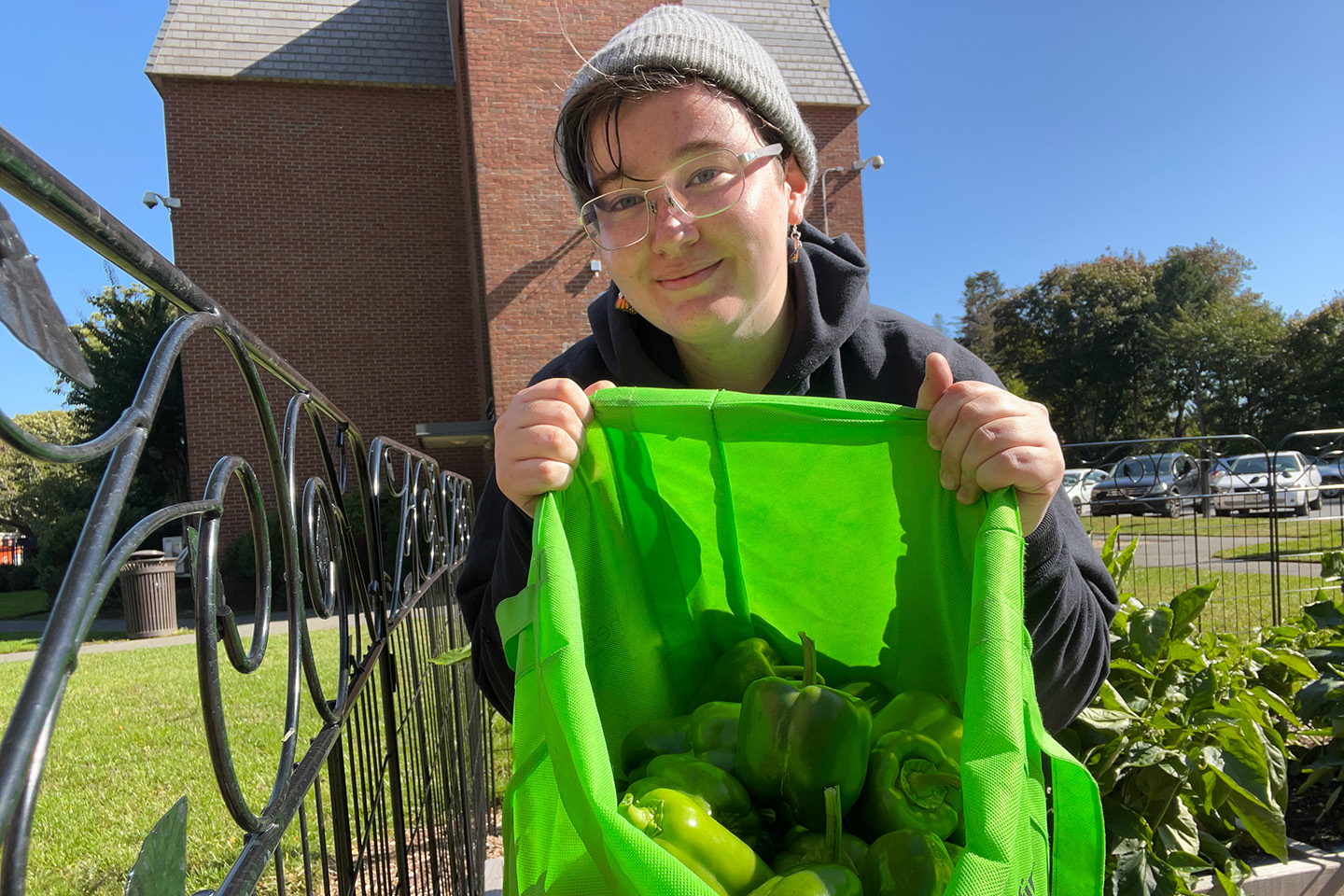 A proud student volunteer showing the bountiful harvest of bell peppers from the Adelphi University community garden.