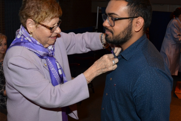 Marilyn Klainberg pinning a Sigma Theta Tau pin to a student's shirt during a ceremony 