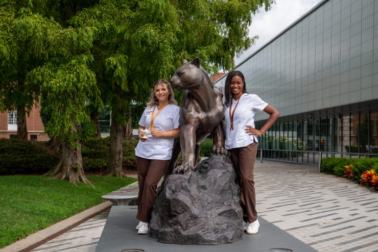 Two nursing students at Adelphi poing near the panther statue