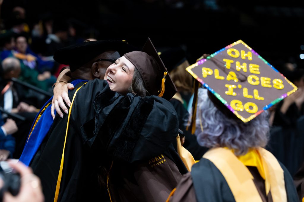 An Adelphi University graduate in cap and gown hugs her professor during the commencement ceremony.