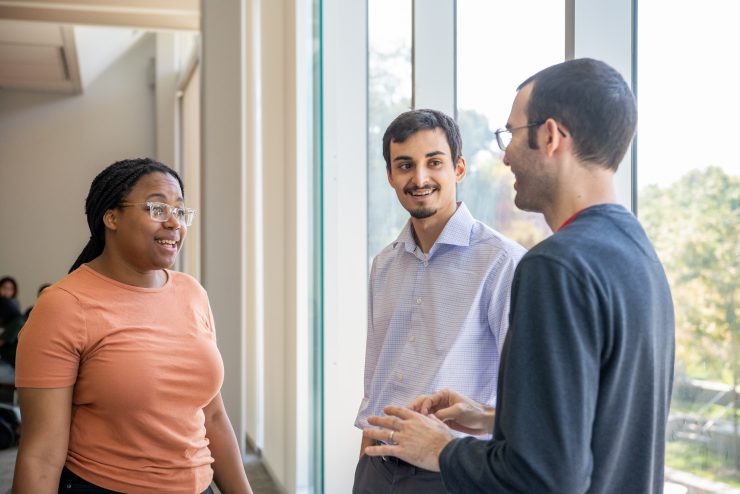 Three graduate students talking in front of a large window on Adelphi's campus