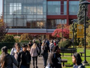 Students walk to and from class on sidewalk in front of a large modern academic building