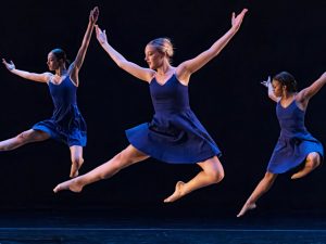 Three women dancers leap in unison, arms overhead.