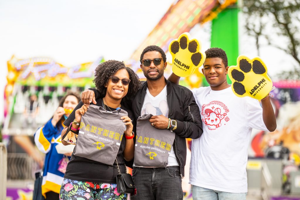 A family holds up Adelphi University shirts and foam paws during our annual Spirit Weekend Carnival.