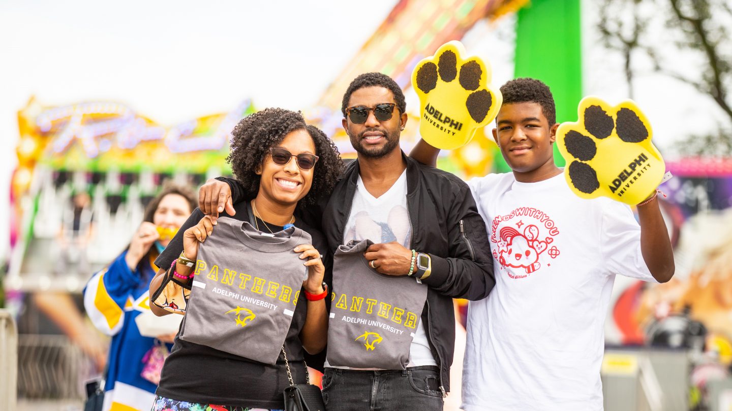 A family holds up Adelphi University shirts and foam paws during our annual Spirit Weekend Carnival.