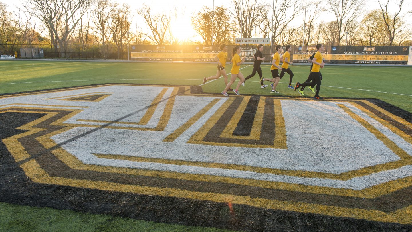 Adelphi athletic runners on the field at sunrise.
