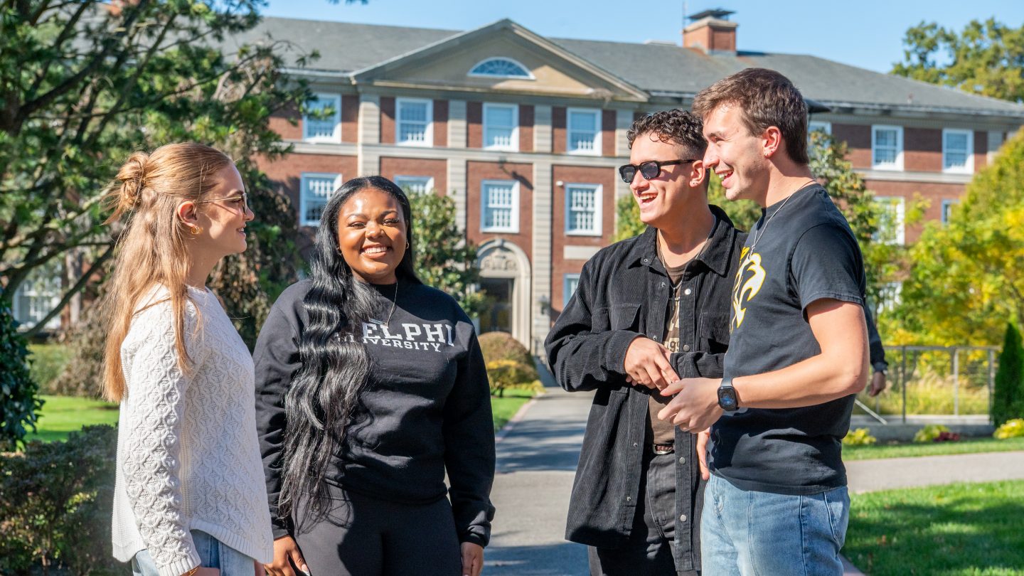 Adelphi students stand outside talking in front of Levermore Hall at Adelphi University