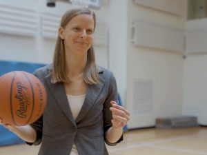 Meredith Whitley, PhD, a professor of health and sport sciences, stands in a gymnasium, holding a basketball.