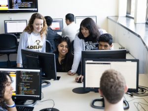 Eight Adelphi students gather around their computer screens, talking excitedly.
