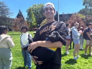 Junior James Tullo holds a black Labrador puppy in his arms, while other students gather in the background.