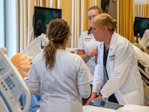 A faculty member and two students at the side of a hospital bed attending to one of the lifelike manikins in the simulation lab.