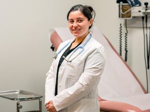 Female nursing graduate student wearing a white lab coat and stethoscope in a medical office.
