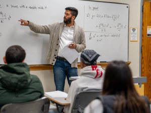 Dr. Venkatesh is seen at the whiteboard at the front of a classroom of students.