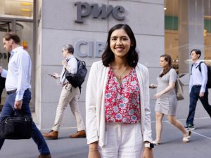 A young woman in business attire poses for the camera on a busy sidewalk in Midtown Manhattan. 