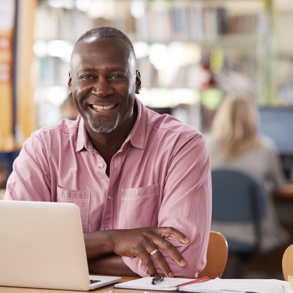 Male smiling student at laptop. Professional going back to college.