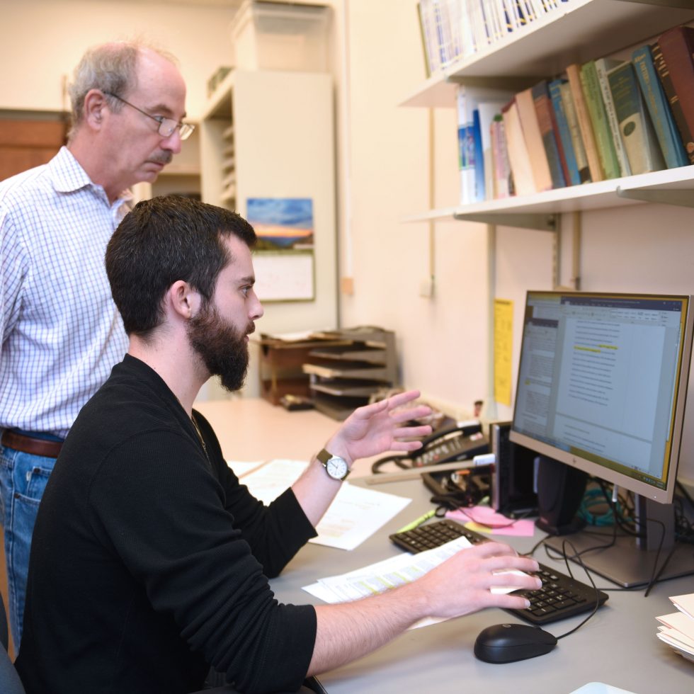 Professor Bornstein listening to a PhD psychology student explain a point in front of a computer with data showing on the screen.