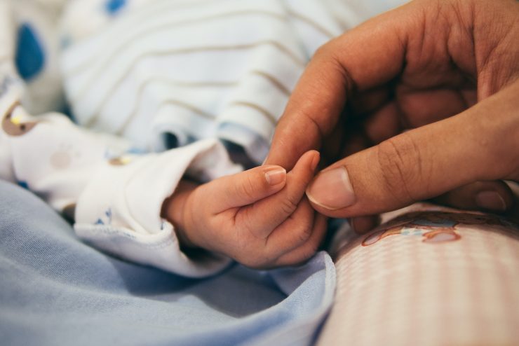 A parent hand holds a tiny infant hand in a loving embrace.