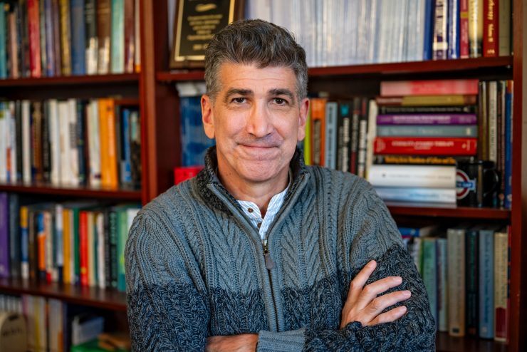 Dean Chris Muran, PhD standing cross-armed in front of a bookshelf