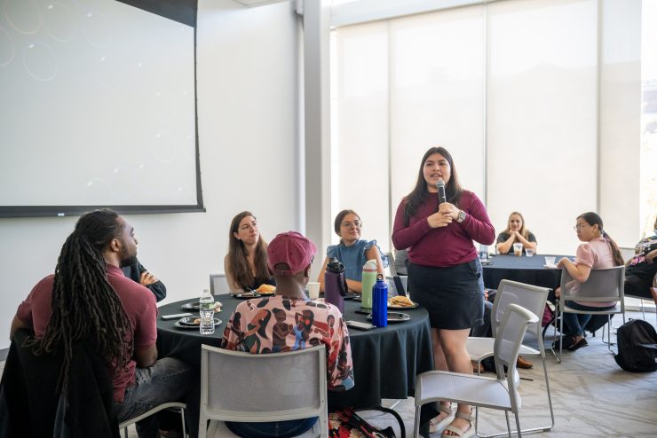 A student speaks confidently into a microphone in front of a room of people.