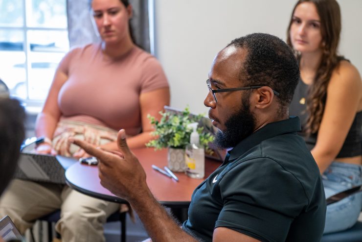 A male psychology student speaks to small PhD group discussion with laptop open.