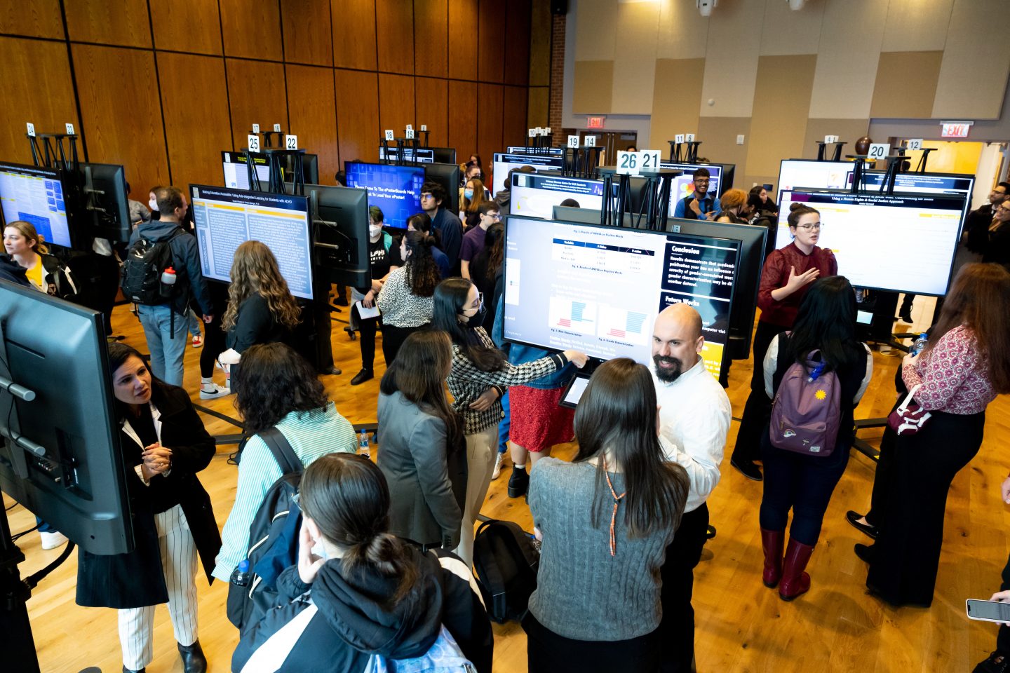 Participants walking around the conference floor where large poster screens are on display.