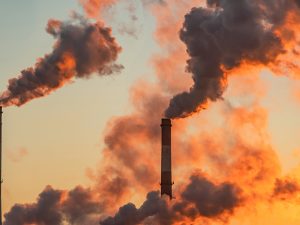 A smokestack at an industrial facility spews gray emissions into a late afternoon sky.