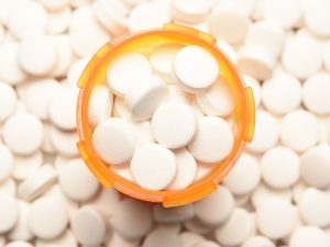 A photo of prescription drugs in a pill bottle. The bottle, seen from above, sits on a table completely covered with the same pills.