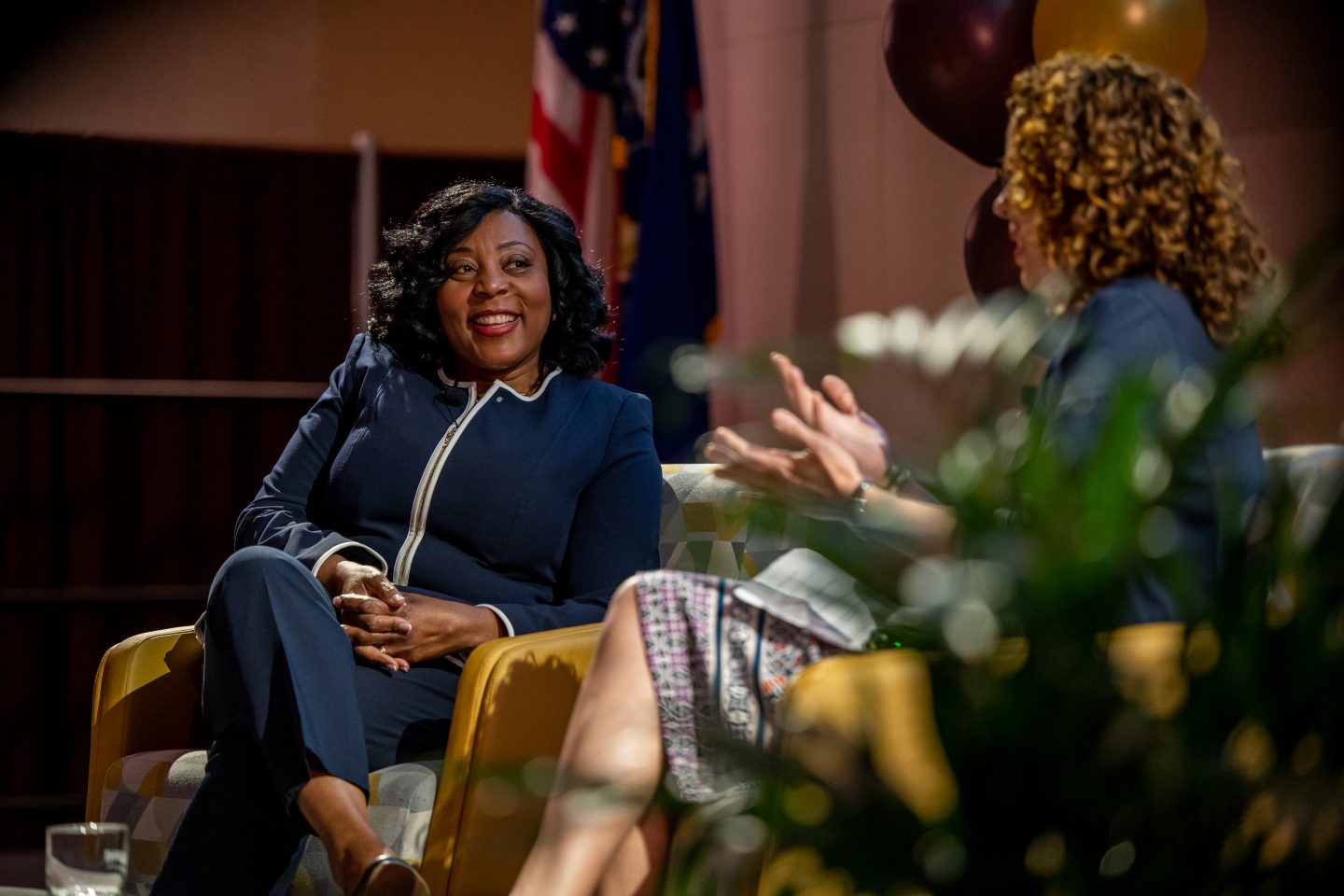 A smiling Francine Conway, the 2023 Scholarship and Creative Works Conference keynote speaker, a Black woman, is seated on a University Center stage being interviewed by a white woman—discussing her role in establishing that annual event two decades ago.