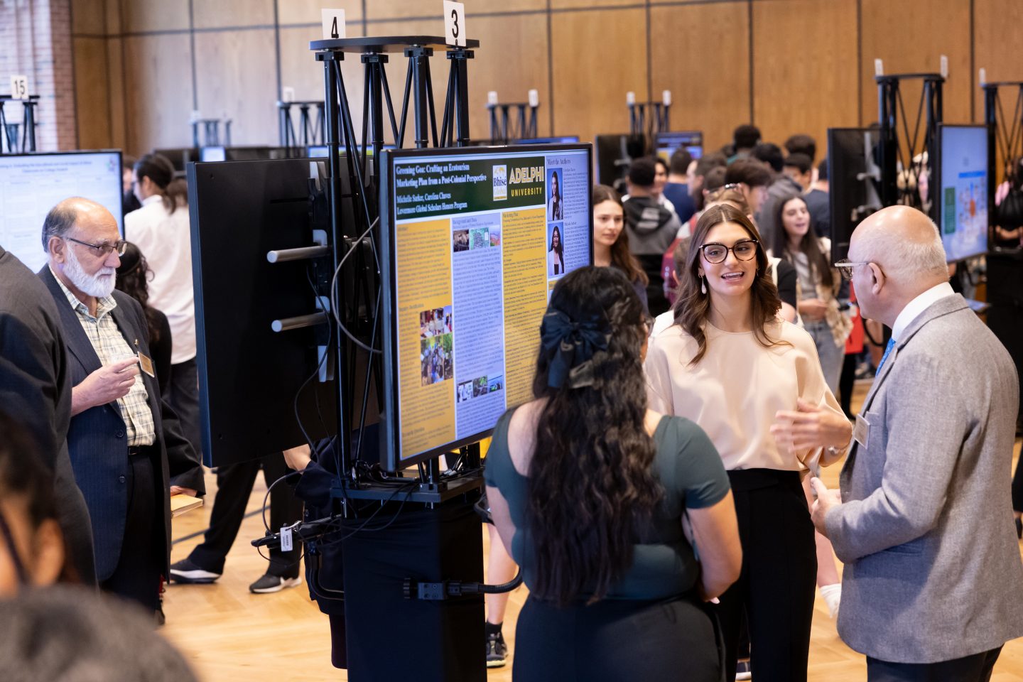 In a large room of e-posters, students and faculty members are seen in discussions about their presentations.   