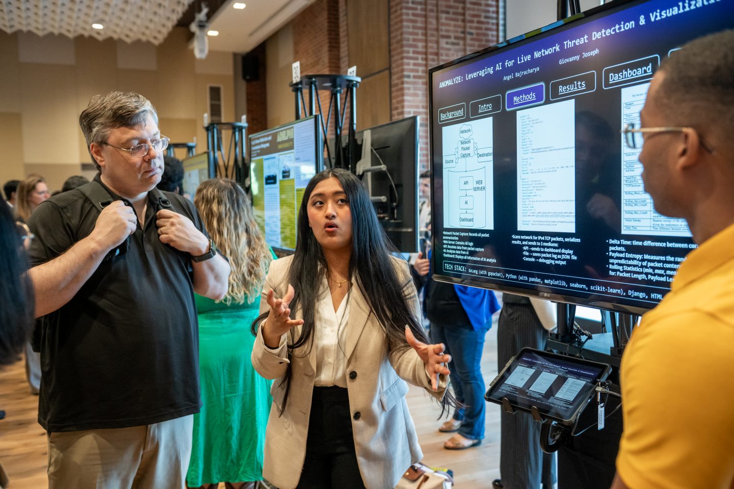Kees Leune, Associate Professor, Chair Mathematics and Computer Science, listens as Angel Bajracharya and Giovanni Joseph present their research on AI in threat detection.