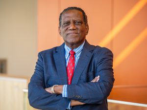 A man standing with his arms crossed in a blue suit and red tie